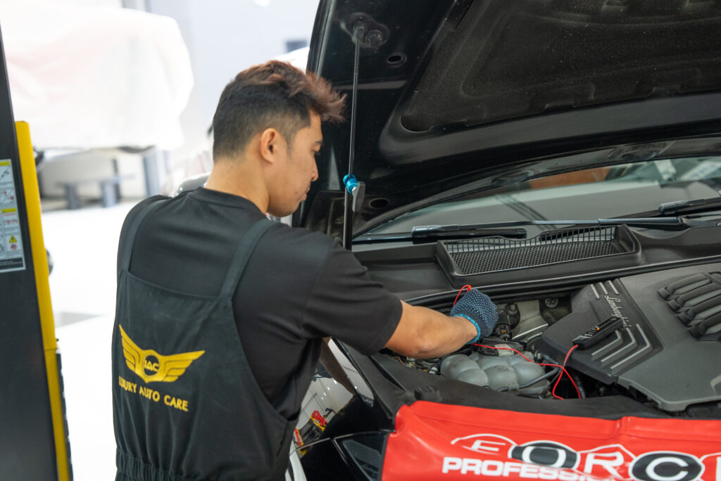 Technician carrying out mechanical and electrical diagnostics on a vehicle engine in a professional workshop